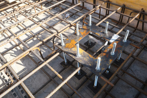 Piastre in acciaio in cantiere edile. Construction site for a building with a steel structure. Plates with anchor bolts for mounting steel columns on a reinforced concrete foundation. - MyVideoimage.com | Foto stock & Video footage