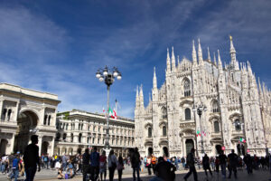 Piazza Duomo Milano. Milan Cathedral facade with flags on blue sky. The facade of the cathedral with many people walking. Flags waving on the blue sky. - MyVideoimage.com | Foto stock & Video footage