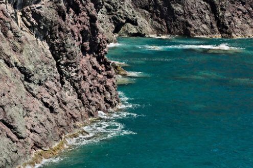 Red rocks an sea. Sea waves break on the rocks of the Ligurian mountain.  Near the Cinque Terre a seascape with blue sea and dark red rocks. Village of Framura. - MyVideoimage.com | Foto stock & Video footage