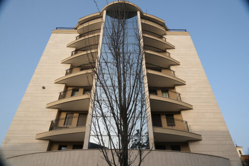 Residential BUilding. Busto Arsizio. Modern tower building set in front of a leafless tree. On the central part of the building you can see the vertical window of the stairwell. - MyVideoimage.com | Foto stock & Video footage