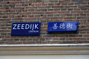 Road sign with written in Dutch and Chinese applied on red brick façade. - MyVideoimage.com