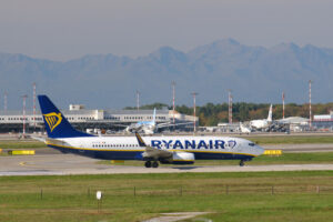 Ryanair Boeing 737-800 airplane on the Malpensa airport runway. In the background the buildings of Terminal Cargo and parked airplanes. - MyVideoimage.com