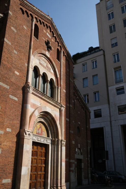 San Babila Milano.  Brick facade of the church of San Babila in Milan. On the facade a mosaic. In the background modern buildings. Milano foto. - MyVideoimage.com | Foto stock & Video footage