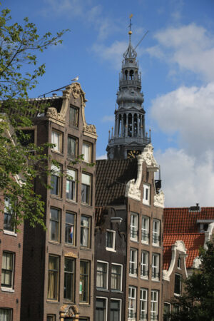 Sloping facade of a brick house. In the background the tower of a bell tower with blue sky and clouds. - MyVideoimage.com