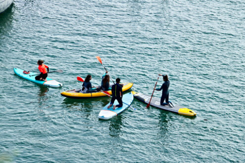 Ragazzi su surf. Some boys and girls paddle on a board on the surface of the sea.