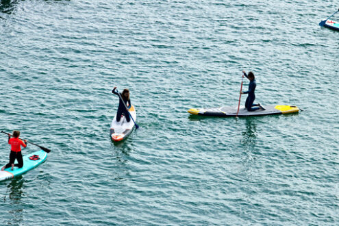 Guys on surf. Some boys and girls paddle on a board on the surface of the sea. View from above.