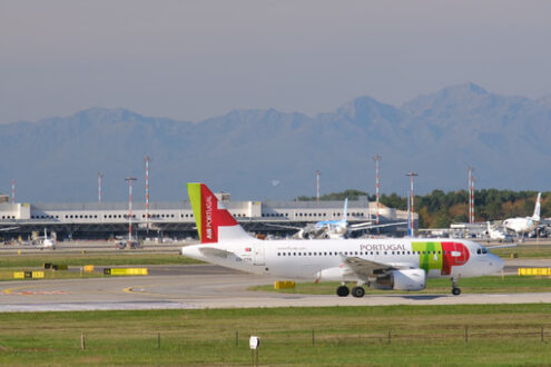 TAP Portugal Airbus A319-112  airplane on the Malpensa airport runway. In the background the buildings of Terminal 1 and parked airplanes. - MyVideoimage.com