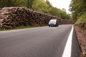 Timber wall stacked along a road where a car passes. - MyVideoimage.com