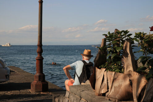 Tourist with hat, sitting watching the blue sea. - MyVideoimage.com