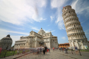 Tourists in Pisa, Piazza dei Miracoli. Piazza dei miracoli of Pisa. Travelers admire architecture. Cathedral, leaning tower of the Tuscan city. Blue sky with clouds. - MyVideoimage.com | Foto stock & Video footage