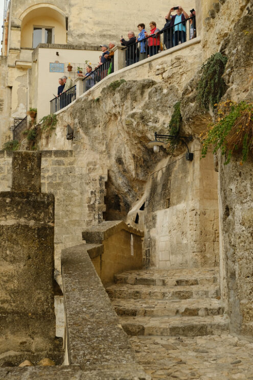 Tourists photograph the landscape. Group of tourists photographing the view from a terrace in the city of Matera. Street with beige-colored tuff stone wall. - MyVideoimage.com | Foto stock & Video footage