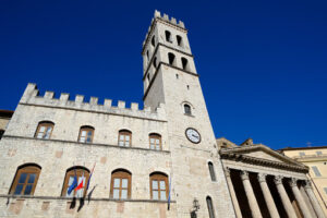 Town hall with flags and clock tower in the square of Assisi. Made with masonry in stone blocks. - MyVideoimage.com