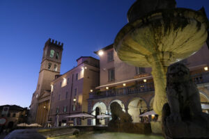 Town square of Assisi with the Torre del Popolo and fountain at night. The city of San Francesco with the lights of the night. - MyVideoimage.com