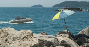Umbrella and motorboat. Colorful beach umbrella on the cliff. Video footage.