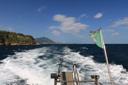 Wake of water left by a ship in the blue sea. In the background the island of Ischia (Naples) with the port and the lighthouse. - MyVideoimage.com