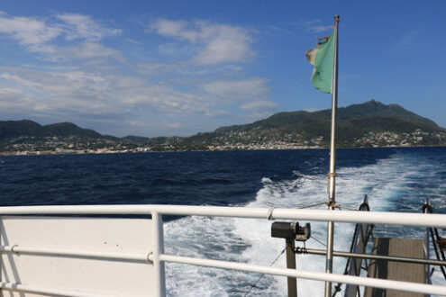 Wake of water left by a ship in the blue sea. In the background the island of Ischia (Naples) with the port and the lighthouse. - MyVideoimage.com