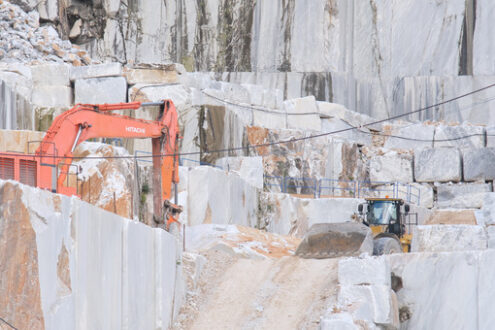 Pala meccanica nelle cave di marmo. Well loader on a steep dirt road in the white marble quarries. In the background the walls with the texture of the marble and a backhoe.