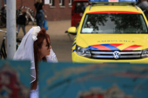 Woman with wedding dress sitting near yellow ambulance. - MyVideoimage.com