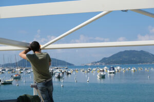 Worker performs maintenance work on a seaside gazebo. Blue sky and sea background with boats. - MyVideoimage.com | Foto stock & Video footage