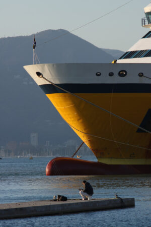 Yellow ship. Bow of a yellow ship anchored in port with a fisherman on the dock. - MyVideoimage.com | Foto stock & Video footage